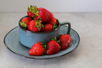 Ripe strawberries in a mug and on a gray ceramic plate.