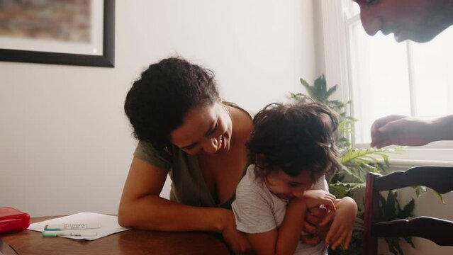 Mother and father play with their son on a homeschooling break, tickling and having fun with him. Parents of a young boy bond and create precious family memories with their son.