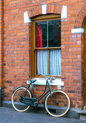 Fototapeta na wymiar Old ladies bicycle leans against redbrick house wall with net sash windows 