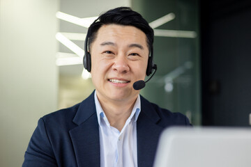 Close-up photo portrait of Asian man with video call headset, tech support worker smiling and...