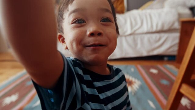 Curious little boy laughing and chatting with someone in an authentic family moment. Adorable young boy having fun as he plays in his parents' room at home, with his face zooming into the camera.
