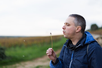 A man blowing a dandelion with the vineyards at the background