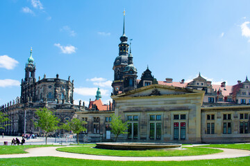 Fototapeta na wymiar Square with old buildings with towers and spires and decorative elements on the facades. Historical architecture. Old town. Sunny day with blue sky and green lawns. Dresden, Germany, May 2023.