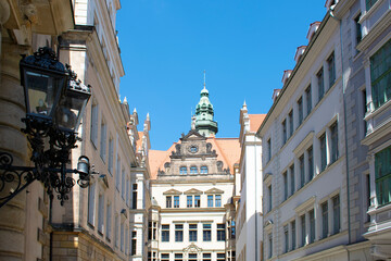 Fototapeta na wymiar View of an old building with tower and red roof, line of facades of buildings and street metal forged lantern. Old architecture. Sunny day with blue sky. Dresden, Germany, May 2023.