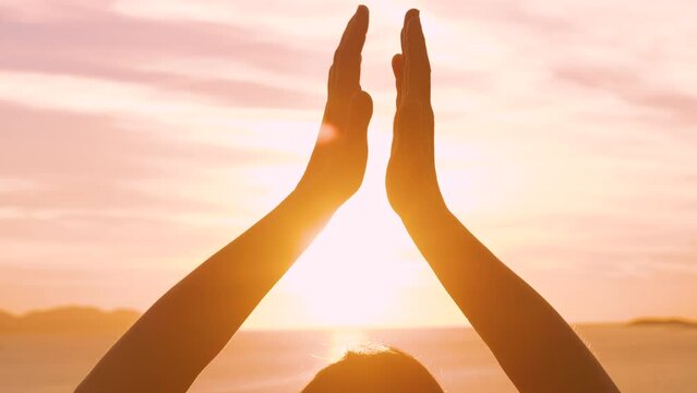 CLOSE UP, LENS FLARE: View of female hands in meditation pose at sunset by sea. She is on a relaxing vacation, practicing yoga in the embrace of stunning Mediterranean seascape on sunny island of Hvar