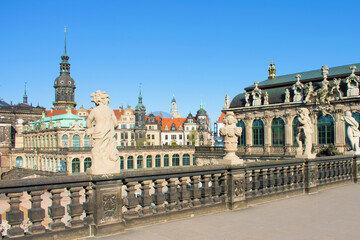 Fototapeta premium View of ancient buildings with towers, spires, red roof, decorative elements and sculptures. Ancient antique fence with statues of boys in the foreground, baroque style. Dresden, Germany, May 2023.