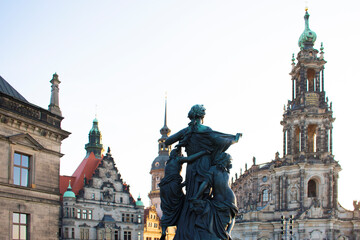 View of an ancient sculpture of a woman against the background of old buildings with tower, spires and red roof. Old historical architecture and art. Dresden, Germany, May 2023
