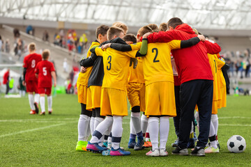 Junior soccer team huddling with a coach at halftime. Teammates standing in a circle at the stadium grass pitch. Sports players motivated to win the final game