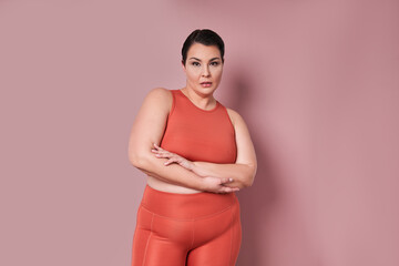 Satisfied plus size woman in fitness wear standing arms crossed at the studio