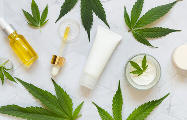 Fototapeta na wymiar Cosmetic bottles, jars and tubes with blank label near green cannabis leaves. Mockup