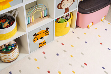 White shelving with colorful storage baskets and boxes with toys. Interior design. Organizing and...