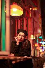 Vertical view of the young stylish brunette sitting in cafe in lights of night city