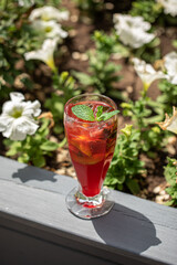 Glass of fresh fruit lemonade with ice and mint in the garden