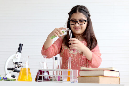 Cute Indian school girl in India traditional dress costume doing science experiments in laboratory, young scientist kid with microscope and lab equipment learning biologics and chemistry in classroom.