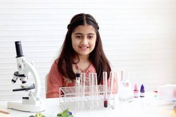 Cute Indian school girl in India traditional dress costume doing science experiments in laboratory, young scientist kid with microscope and lab equipment learning biologics and chemistry in classroom.