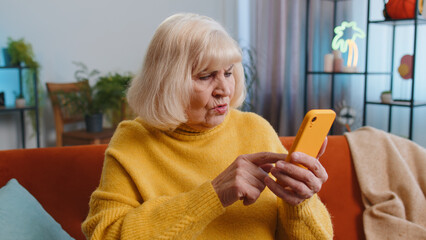 Sad displeased senior grandmother use smartphone typing browsing, loses becoming surprised sudden...