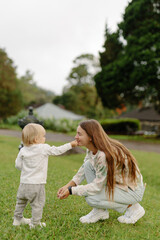 Little girl child gives mom a sniff of a flower or grass petal while sitting on a green lawn with a beautiful view of the nature garden. Family outdoor recreation, happy family