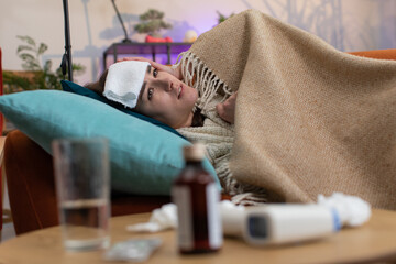 Young ill woman suffering from cold or allergy sitting on sofa in living room at home. Sick girl...