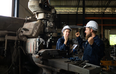 Naklejka na ściany i meble Both of mechanical engineers are checking the working condition of an old machine that has been used for some time. In a factory where natural light shines onto the workplace