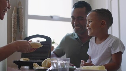 Cheerful mixed race family making breakfast while husband and little son eating and drinking juice at kitchen table
- Powered by Adobe