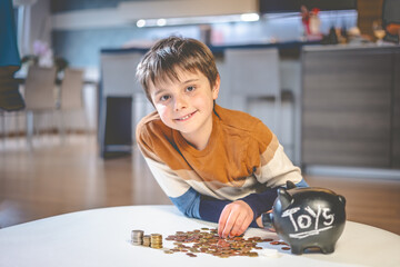 Portrait of a young, smiling, caucasian kid sitting by a living room coffee table, counting his...