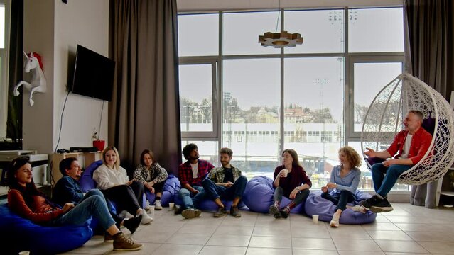 Office workers are sitting in the room on cushion chairs and discussing something. Business partners hold a meeting in a relaxation room.