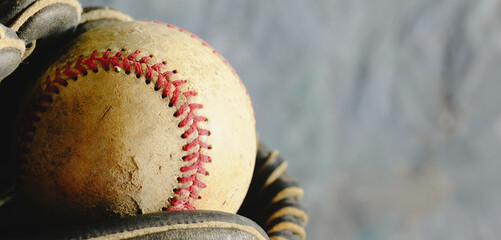 Baseball background with old ball in glove against blurred gray background.