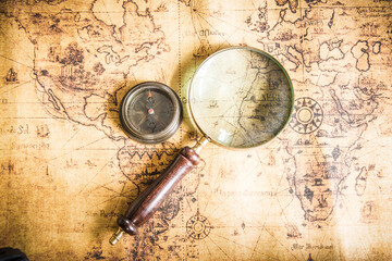 Fototapeta na wymiar Old vintage retro compass and magnifying glass on ancient map.The map used for background is in Public domain.