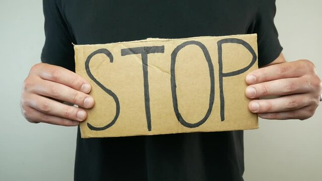 A young man is holding a cardboard sign with the word stop.