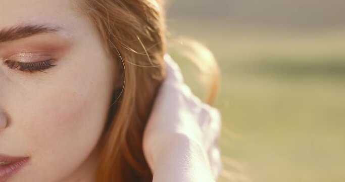 Close up face of red-haired young woman with long silky luxurious healthy well-groomed hair. Red well-groomed healthy female hair. Woman touching red healthy long hair at golden sunset close up.