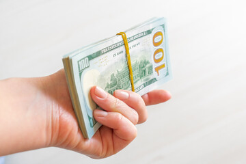 A stack of one hundred dollar bills is held by a woman's hand. A stack of one hundred dollar bills...