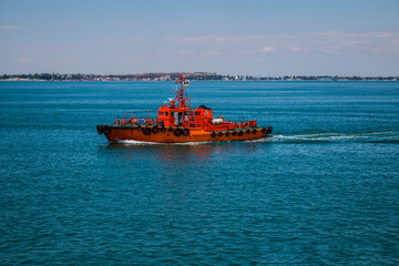 A small red boat sails in the clear blue sea