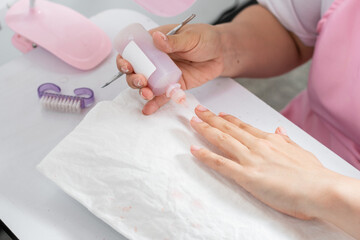 close-up of the hands of a young woman applying liquid nail polish remover to her nails