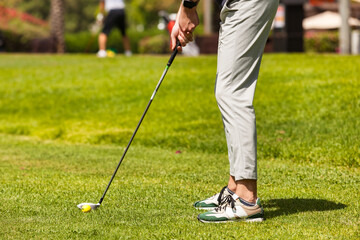 Close-up of legs golfer young man with golf club getting ready to hit ball in golf course at...