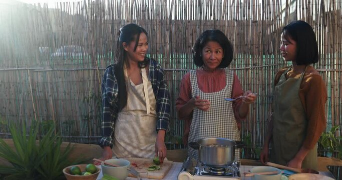 Asian family preparing together traditional thai food at house backyard - Mother tasting spicy mushroom soup