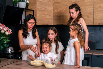 Young mother cooking sweet cheesecake with four her daughters at home.