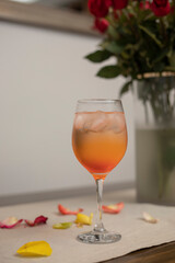 An alcoholic drink served in a glass, on the table with rose petals and a bouquet in the background