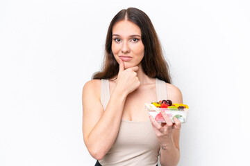 Young caucasian woman holding a bowl of fruit isolated on white background thinking