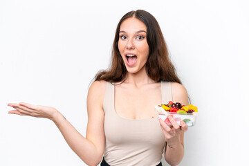 Young caucasian woman holding a bowl of fruit isolated on white background with shocked facial expression