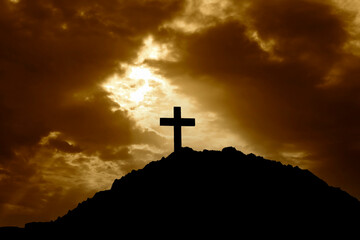 Silhouette of a cross on top of a mountain at sunset. With the suns rays shining down on the cross