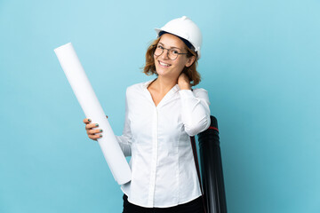 Young architect Georgian woman with helmet and holding blueprints over isolated background laughing