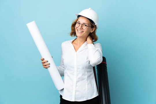 Young architect Georgian woman with helmet and holding blueprints over isolated background laughing