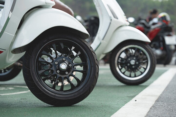 Close-up of wheels of a scooter motorcycle parked on a beautiful road in the daytime.