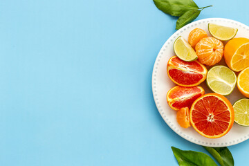 Plate full of fresh citrus fruits with green leaves, top view