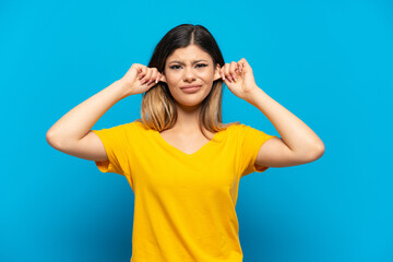 Young Russian girl isolated on blue background frustrated and covering ears