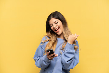 Young Russian girl isolated on yellow background with phone in victory position