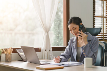 Professional millennial Asian businesswoman in casual attire is making a business call while...