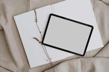 Flat lay of tablet with blank screen. Copy space mock up. Aesthetic dried grass on beige crumpled...