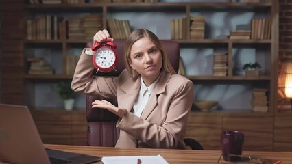 Angry company director warning colleague for being late at work. Young woman demonstrating red alarm clock and asking for being punctual and always coming to office on time.