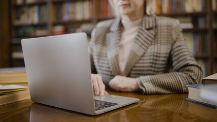 Close-up of senior woman using a laptop to work, professor sitting in the library